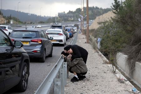 Israelis take shelter at the side of a highway as a siren sounds following a missile attack from Iran on Israel, near Abu Ghush